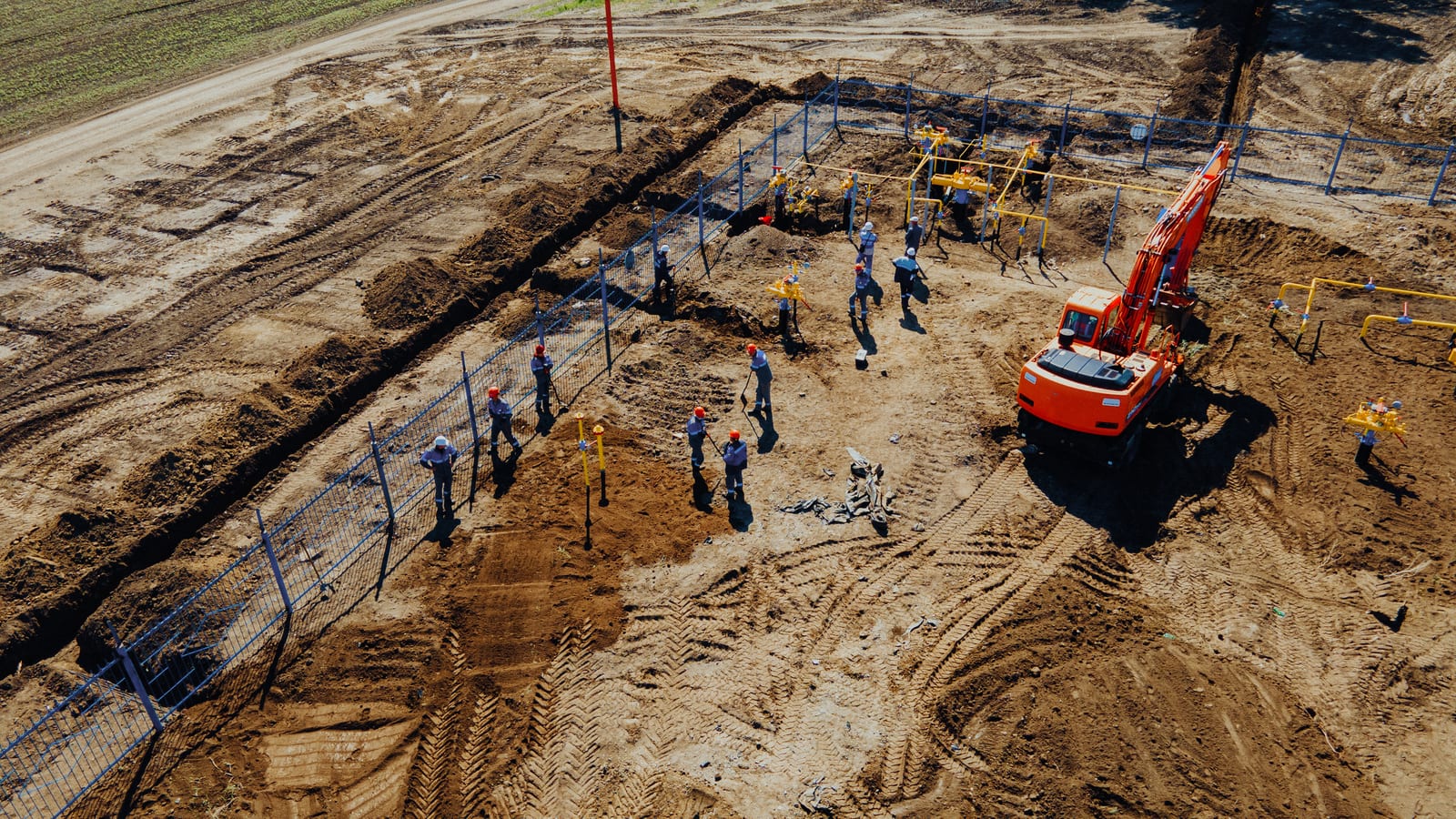 Construction workers and an excavator beside a pipe trench